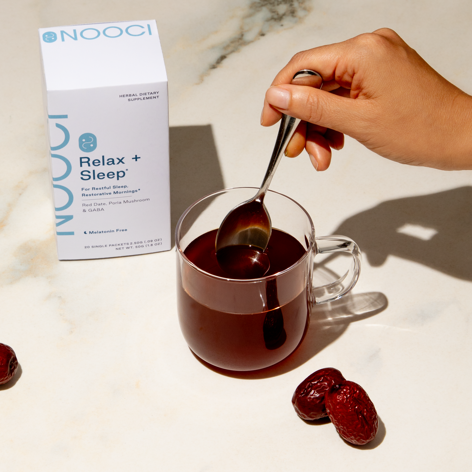 Person stirring a cup of dark liquid with a spoon, next to a box labeled 'NOOCI Relax + Sleep'.
